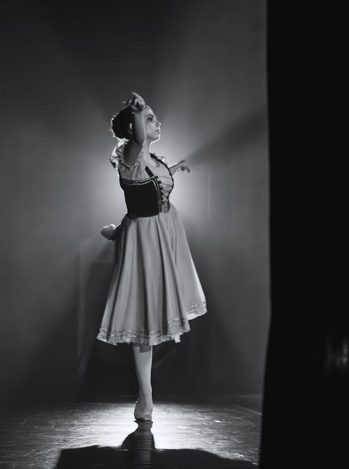 Black and white image of a ballerina gracefully posing on stage with dramatic lighting.